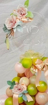 Flowers on top of a Transparent bubble resting on 15 light pink and green balloon tied with pink ribbons and roses inserted in between the balloons
